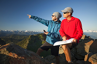 Two men use a paper map and a compass to identify nearby peaks while hiking in the North Cascade Mountain Range, North Cascades National Park, Washington, United States of America