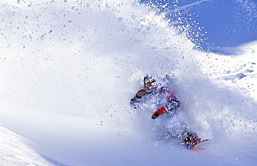 A man slashes deep snow on his snowboard and comes through the resulting powder cloud.