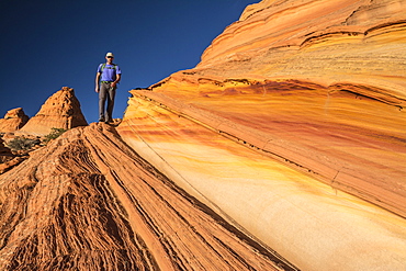 A man hiking along sandstone layers, South Coyote Buttes, Vermillion Cliffs National Monument, Kanab, Utah.