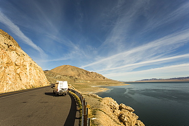 A white van with bikes on the back in a large paved pullout overlooking a large blue lake in a vast, sunny desert landscape.