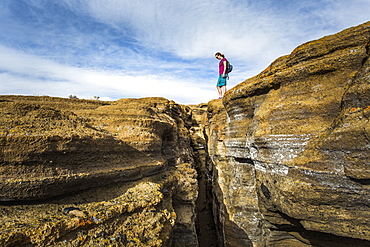 A young woman stands at the edge of a deep slot canyon.