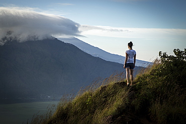 Woman standing on mountain overlooks volcano at sunrise on Bali