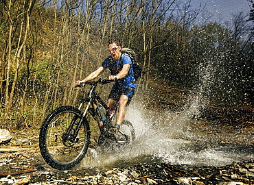 Guy rides his mountain bike over mountain stream. Image captured at the moment of a biggest splash. Taken on Gledic mountains near Kragujevac, Central Serbia at a sunny Spring day.