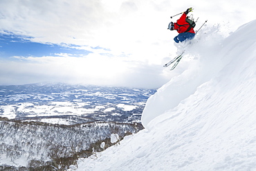 A male skier is jumping in the air onto a slope with deep powder snow in the ski resort Niseko United on the Japanese island of Hokkaido.