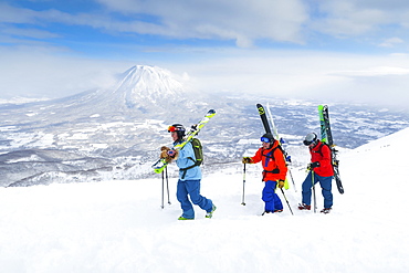 With the volcano Yotei in the background a female and two male backcountry skiers are hiking to the summit of mount Annupuri, in the ski resort Niseko United on the Japanese island of Hokkaido. Niseko United is comprised of four resorts on the one mountain, Annupuri (1,308m). 100km south of Sapporo, Niseko Annupuri is a part of the Niseko-Shakotan-Otaru Kaigan Quasi-National Park and is the most eastern park of the Niseko Volcanic Group. Hokkaido, the north island of Japan, is geographically ideally located in the path of consistent weather systems that bring the cold air across the Sea of Japan from Siberia. This results in many of the resorts being absolutely dumped with powder that is renowned for being incredibly dry. Some of the Hokkaido ski resorts receive an amazing average of 14-18 meters of snowfall annually. Niseko is the powder capital of the world and as such is the most popular international ski destination in Japan. It offers an unforgettable experience for all levels of skier and snowboarder. Mount Yotei in the background is often referred to as the "Mount Fuji of Hokkaido".