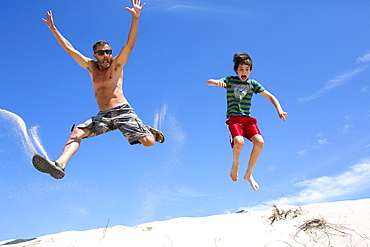 A man and boy jump on a sand dune in Provincetown, MA.