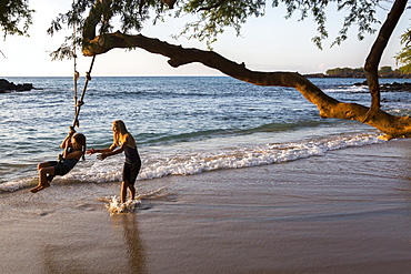 Children play with a rope swing on Waialea beach on the Big Island of Hawaii.