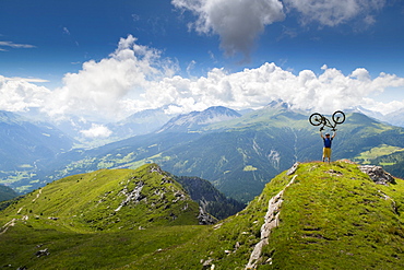 Distant View Of Mountain Bike On Summit Of Mountain Lifting Mountain Bike Above His Head