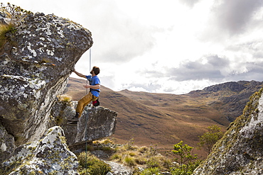 A Male Climber Looks At A Climb And Tests The Quality Of The Rock While Hanging From A Rope