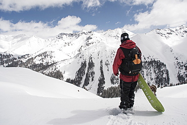 Man Standing With His Snowboard Looking Over Avalanche Paths At Silverton Mountain