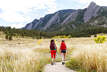 Two Female Hikers Walking On A Trail Beneath The Flatirons In Colorado