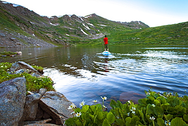 Young male paddleboarding on a high alpine lake in the spring at sunset