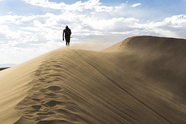 A hiker walking a ridge line in the sand dunes