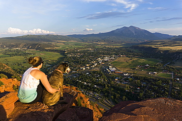 Young female and her dog overlooking a mountain and town at sunset