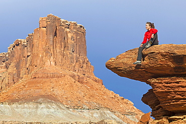 A woman sits on a bedrock terrace at Saddle Horse Bottom below tall canyon walls in Canyonlands National Park, Utah.