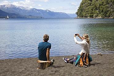 Mature couple take photo on beach by mountain lake