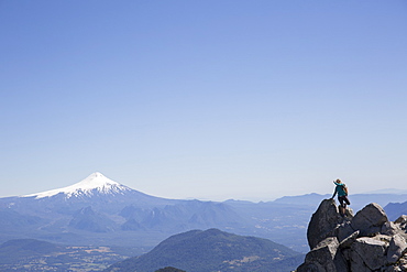 Hiker climbs boulder with snow capped volcano behind