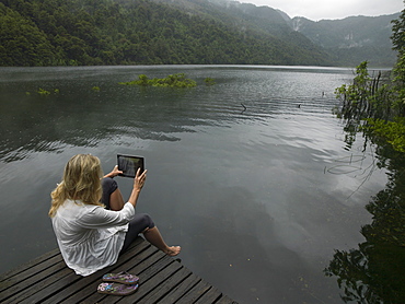 Woman takes photo with tablet on dock in mountain lake