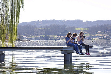 Teen girls take photos from end of pier on lake