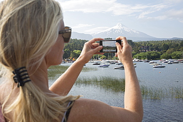 Woman takes smart phone pic over lake, Villarica volcano