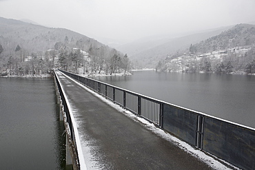 One lane bridge span mountain lake, distant hills and storm