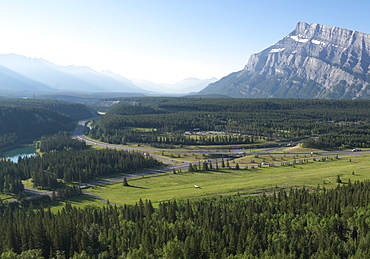 Elevated view down u-shaped valley with river, forest and mountains, airport and highway