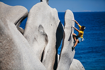 Man climbing on rock near sea, Capo Testa, Sardinia, Italy