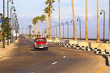 Classic Car Driving Along The Malecon Seawall In Havana's Harbor, Cuba