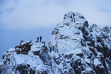 Hikers stand on steep snowy ridge near Tatind, Vestvågøy, Lofoten Islands, Norway
