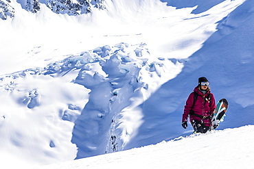 Professional Snowboarder Helen Schettini hikes to a ridge with a glacier in the background on a sunny day in Haines, Alaska.