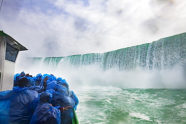 A boat of tourists huddle under blue plastic ponchos to keep the drenching waterfall spray off as the boat, ?Maid of the Mist? brings them to the base of Niagara Falls, on the Niagara River.