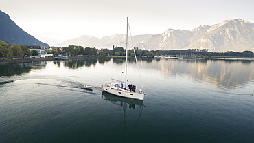 aerial view on a sailing boat and rescue boat crossing the Geneva Lake, with mountains in the background, trees on the lake's banks and a marina in Villeneuve, Vaud Canton, Switzerland