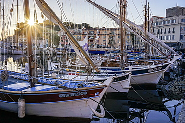 winter sunset over the harbor of Sanary-sur-Mer in the South of France with several boats docking, among which three wooden boats in the foreground of the picture.