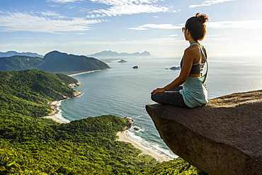 Woman sitting on the edge of the mountain in Pedra do Telégrafo, Barra de Guaratiba, west side of Rio de Janeiro, Brazil