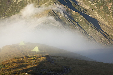 Tents in alpine environment engulfed by fog at sunrise