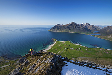 Female hiker enjoys view of beaches and coast from summit of Flakstadtind mountain peak, Flakstadøy, Lofoten Islands, Norway