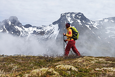 Female hiker hiking through cloudy weather towards summit of Volandstind mountain peak, Flakstadøy, Lofoten Islands, Norway