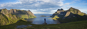 Female hiker takes in panoramic view over Reinefjord and surrounding mountains, near Vindstad, Moskenesøy, Lofoten Islands, Norway