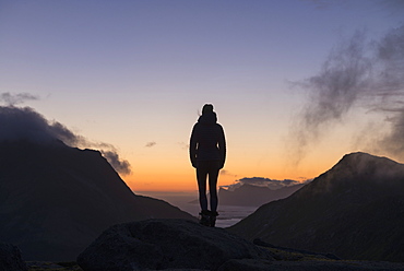 Silhouette of female hiker looking over 3:00am dawn twilight in late summer, Moskenesøy, Lofoten Islands, Norway