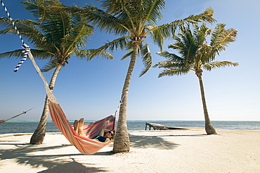 A Young Woman relaxes in a hammock on the beach with a view of the ocean horizon