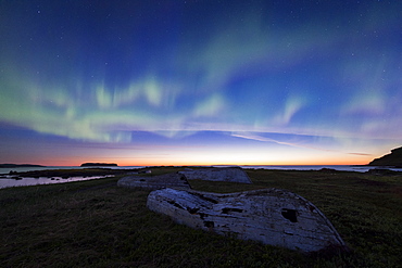 The Northern Lights over old wooden boats in the Norstead Viking replica village in Newfoundland.