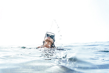 girl in a swimsuit and diving googles playing with the waves on the beach