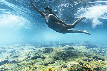 girl in a swimsuit and diving googles playing with the waves on the beach