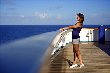 A young woman looks over the railing on the deck of a cruise ship