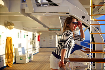 A young woman leans over the railing on the deck of a cruise ship