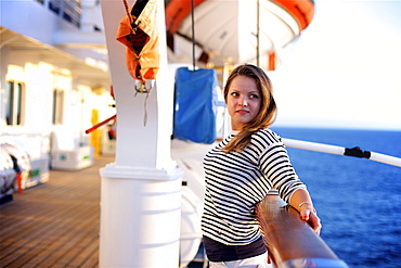 A young woman leans against the railing on the deck of a cruise ship