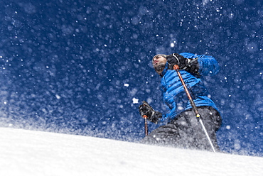 A low angle shot of a man snowshoeing with ski poles in the blowing snow.