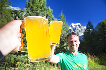 Two hikers are cheering with big local beers in the garden of the Arolla Kurhaus in the Swiss Alps. It is one of the places you can stay for the night half way the Haute Route, a classic multi day hike between Chamonix in France and Zermatt in Switzerland.