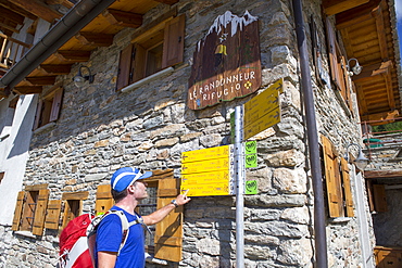 A hiker is looking at a sign post near Courmayeur, half way the Tour du Mont Blanc, a classic multi day hike around the highest mountain of the European Alps. The trek takes about 10 days and goes through France, Italy and Switzerland.