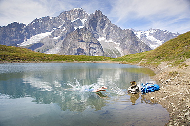 A male hiker is taking a bath in a mountain lake near Courmayeur in the Italian Alps, with Mont Blanc in the back ground. This is halfway the Tour du Mont Blanc, a classic trekking that goes through France, Italy and Switzerland.